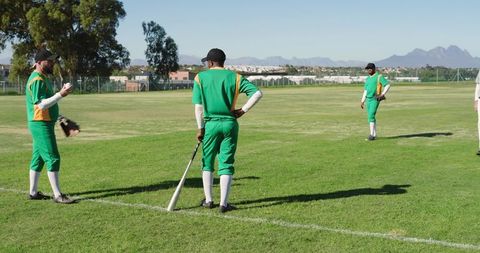 Cricket team preparing on sunlit outfield in green yellow uniforms holding bat and ball