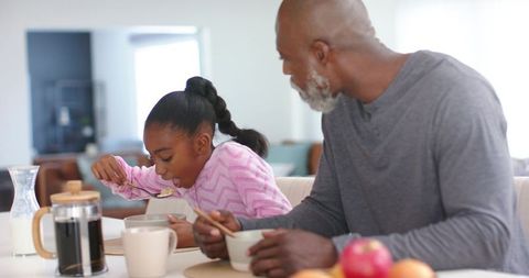 Sunlit african american father and daughter sharing breakfast at modern kitchen table