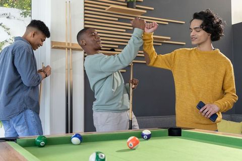 Diverse teen friends celebrating pool win while fist bumping in bright gameroom