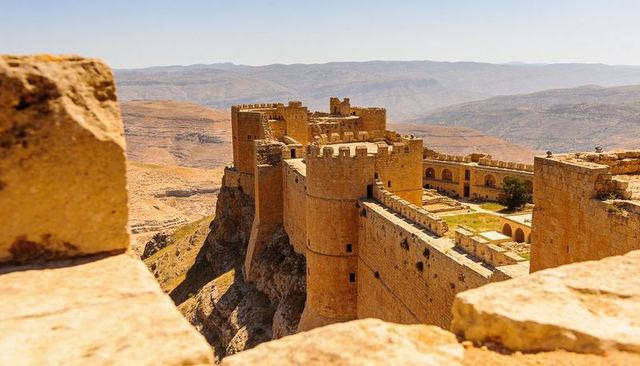 Medieval fortress clinging to cliff, rounded towers, arched courtyard, desert plateau