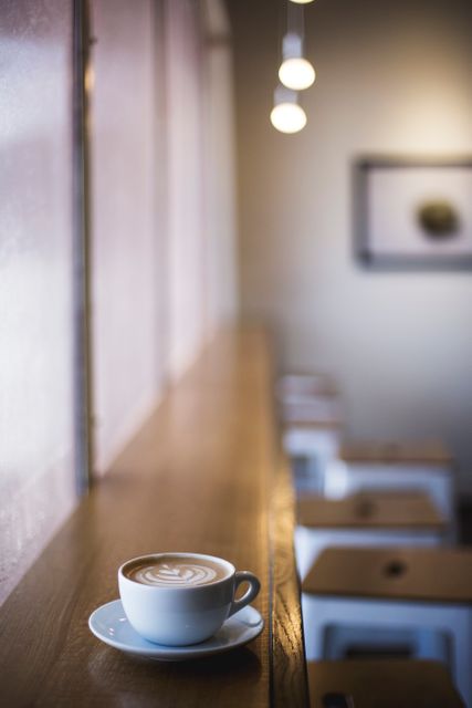 Cafe scene with a latte on a wooden table near a large window. Ideal for promoting coffee shops, relaxation, cozy atmospheres, and warm moments. Perfect for social media, websites, or ads related to cafes, beverages, or quiet spaces.