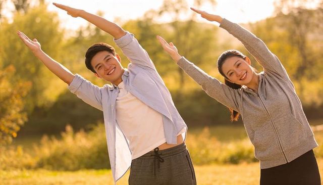 Couple stretching together in sunlit park during golden hour for outdoor fitness wellness