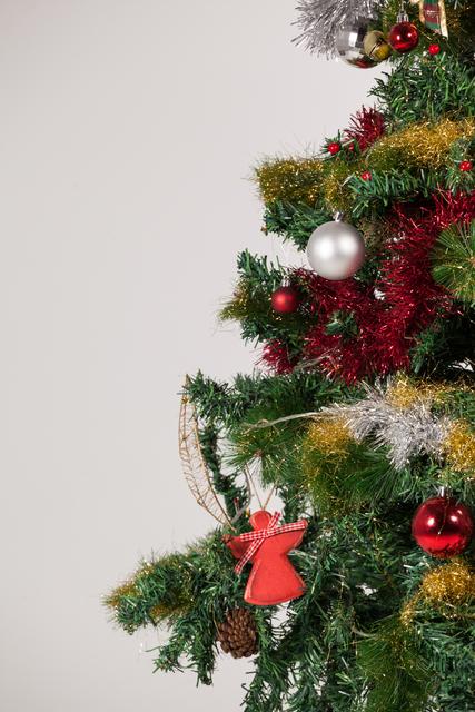 This close-up of a decorated Christmas tree features various ornaments, including baubles, tinsel, and a red angel decoration. The festive colors of red, green, silver, and gold create a joyful holiday atmosphere. This image is perfect for use in holiday greeting cards, festive advertisements, seasonal blog posts, or any Christmas-themed projects.