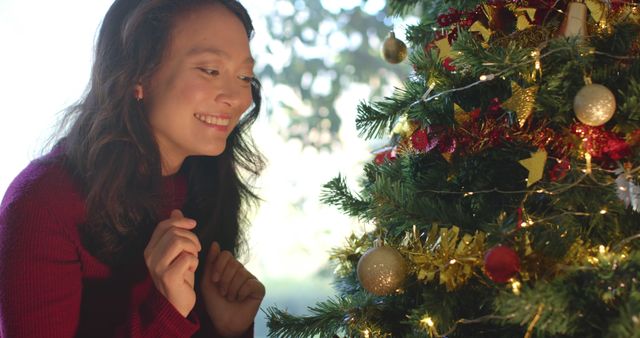 Happy biracial woman decorating christmas tree and smiling, slow motion. Christmas, tradition, celebration, domestic life and lifestyle, unaltered.