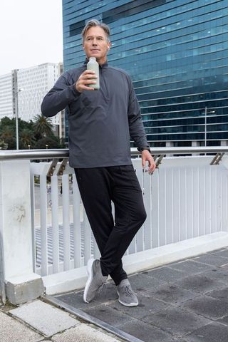 Middle-aged man leaning on bridge railing drinking water after workout in urban skyline