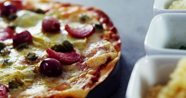 Ideal for menu designs, food blogs, and culinary magazines. This image features a mouth-watering close-up of a freshly baked pizza topped with melted cheese, olives, pepperoni, and capers, capturing its delicious and vibrant appearance.