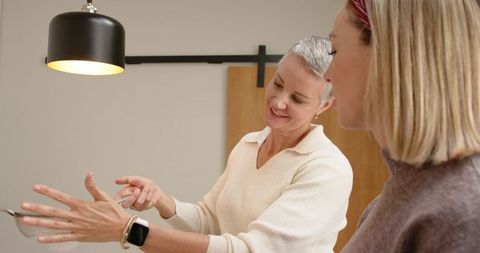 Mature woman demonstrating kitchen utensil to friend in modern minimalist kitchen