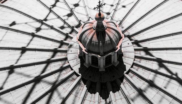 Top-down cupola casting dramatic radial shadows across cathedral dome with cross finial