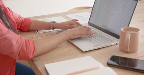 Woman Typing on Laptop at Wooden Desk with Papers and Coffee Mug