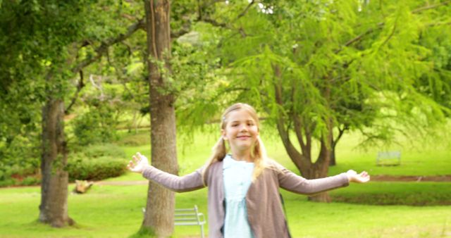 Happy girl spending time in park, surrounded by green trees. Ideal for concepts of outdoor activities, childhood, nature, and happiness. Perfect for advertisements, family-oriented promotions, and educational materials.