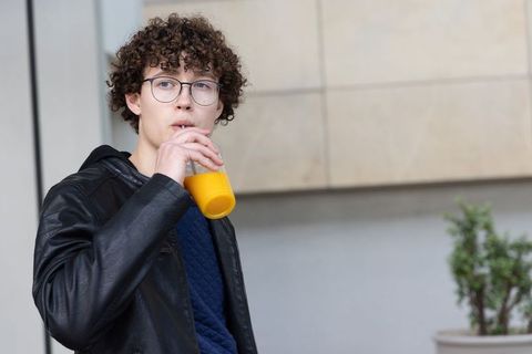 Teenager drinking orange juice outdoors wearing leather jacket and glasses