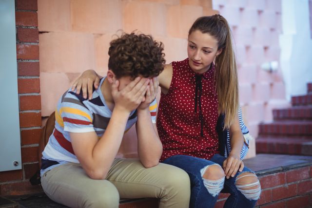 Teen girl consoling her sad friend at school. This image can be used in articles or campaigns about teenage mental health, peer support, and the importance of friendship. It is also suitable for educational materials and counseling resources.