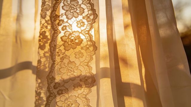 Golden sunlight streaming through floral lace curtains casting warm window shadows
