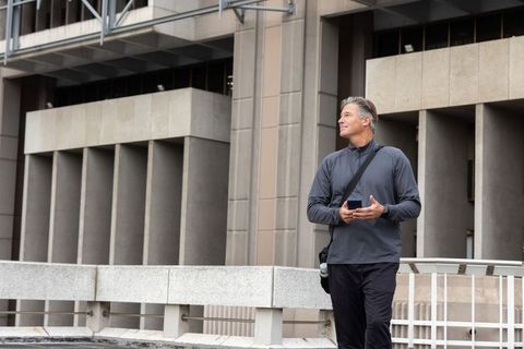 Middle-aged man checking smartphone on elevated urban walkway by modern office building