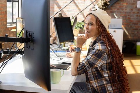 Focused woman in loft office using dual monitors