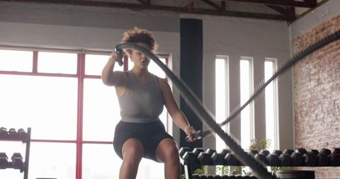 Woman performing seated battle ropes workout in sunlit industrial loft gym for strength
