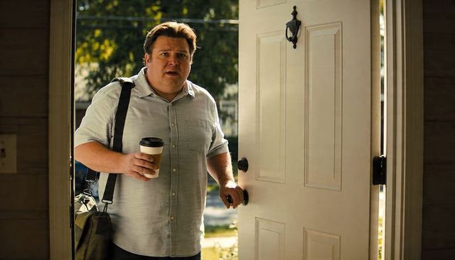 Backlit morning arrival: man entering home holding coffee cup and carrying duffel bag