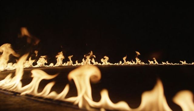 Flickering line of flames reflecting on metal trough against black background