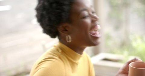 Joyful Woman Laughing with Warm Mug in Sunlit Setting