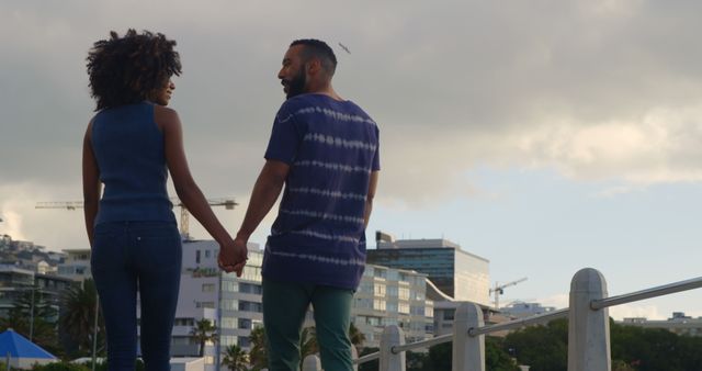 Romantic diverse couple walking with holding hands and talking on sunny promenade, copy space. Summer, vacation, romance, love, relationship, free time and lifestyle, unaltered.