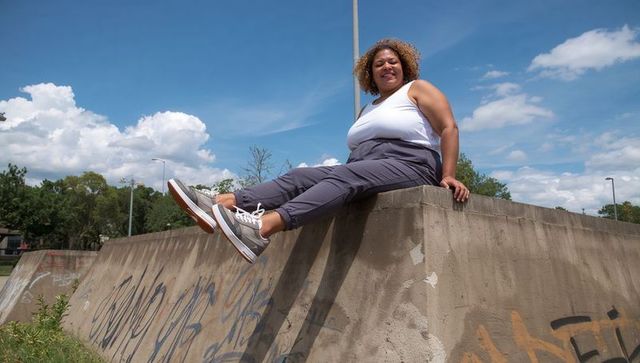 Curvy woman sitting on graffiti wall enjoying sunny urban day in white tank and gray sneakers