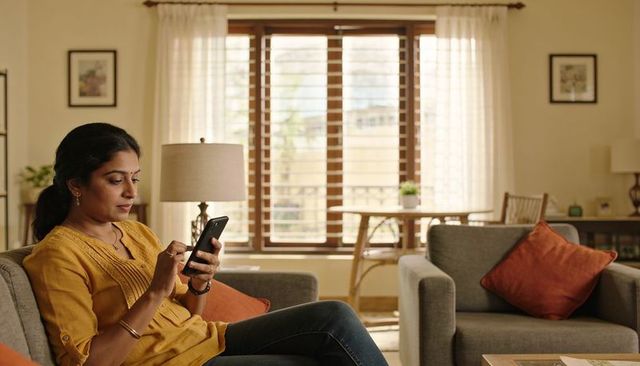 Woman using smartphone on sofa in cozy living room wearing mustard kurta and jeans