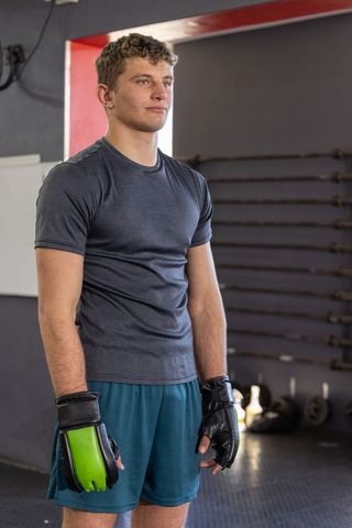 Young boxer standing focused in gym wearing green gloves and athletic training gear