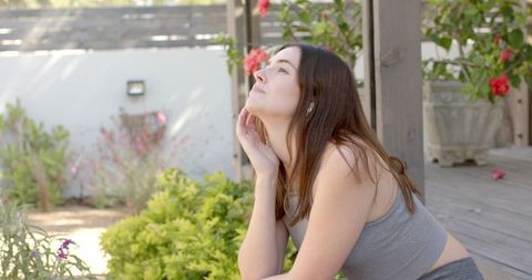 Woman with Earbuds Meditating on Deck in Tranquil Backyard Garden