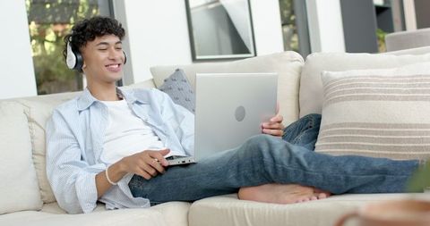 Young Male Relaxing with Laptop and Headphones on Sofa