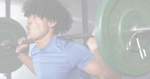 Man performing heavy back squat with barbell and green plates in gym