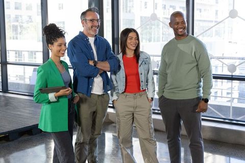 Diverse team standing and smiling in modern office by floor-to-ceiling windows