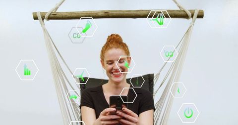 Redhead woman smiling in hammock using smartphone with green eco tech hexagon ui overlay