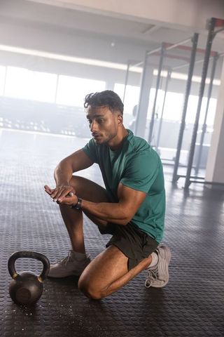 Kneeling athlete preparing kettlebell lift with chalk dust on hands in industrial gym