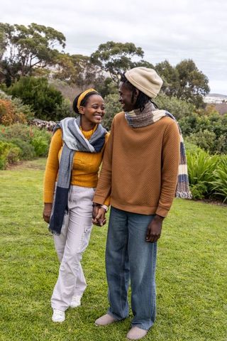Couple walking hand-in-hand on garden lawn wearing cozy autumn scarves and knit sweaters