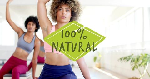 Woman stretching and raising arm in bright fitness studio with 100% natural badge