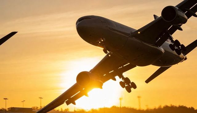 Wide-body jet climbing at sunset showing landing gear down and dramatic golden backlight