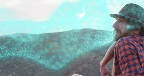 Leaning man gazing over mountain ridges with turquoise digital particle overlay