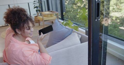 Woman using smartphone voice function seated on sofa near garden window