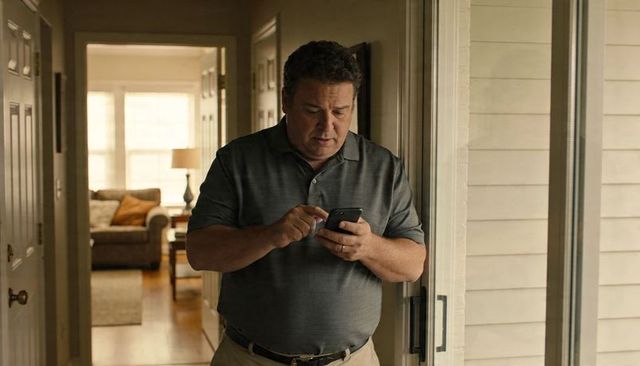 Middle-aged man using smartphone in sunlit home hallway near sliding glass door