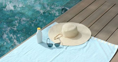 Straw sun hat and sunglasses resting on light blue towel by turquoise pool