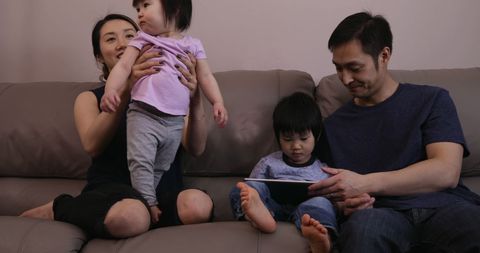 Asian Family Bonding in Living Room with Tablet and Playful Toddler