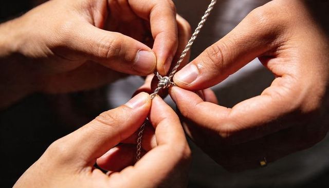 Adult hands untangling knotted silver chain necklace closeup, delicate jewelry clasp repair