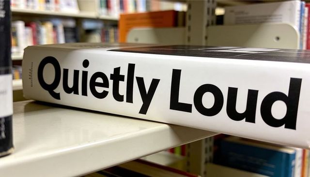 Quietly loud book on shelf, bold black typography on white spine, low-angle closeup
