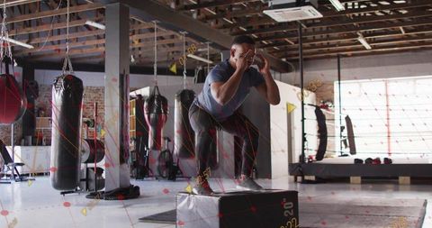 Athlete landing plyometric squat on 20-inch plyo box in industrial boxing gym