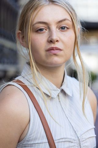 Blonde woman facing camera on urban walkway wearing sleeveless top and leather bag