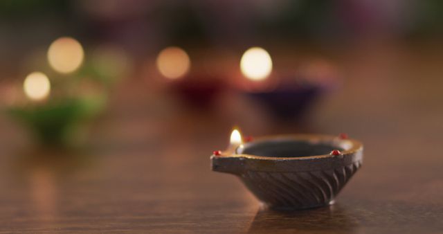 Lit candles in decorative clay pots on wooden table top, focus on foreground one, bokeh background. diwali festival, celebration, tradition and ceremony concept.