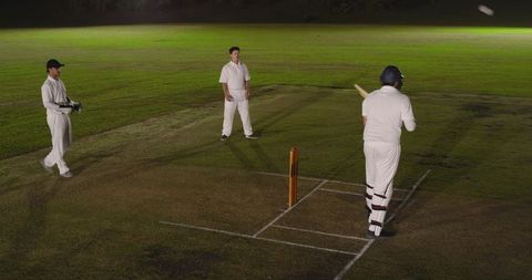 Floodlit night cricket match with batsman preparing at crease and fielders standing ready