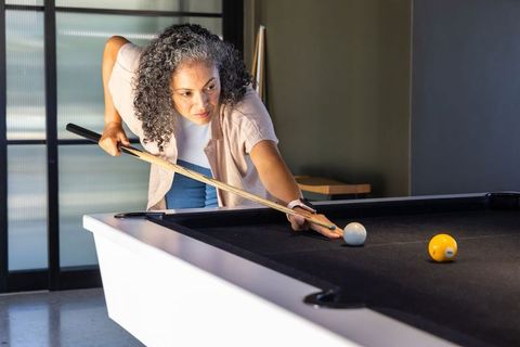 Senior african american woman playing pool on black-felt table, focused concentration
