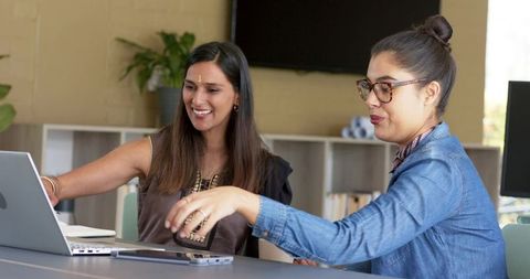Diverse female colleagues collaborating and pointing at laptop during coworking meeting