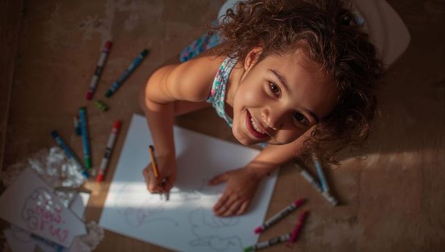 Smiling child drawing on floor with markers and pencil in warm sunlight